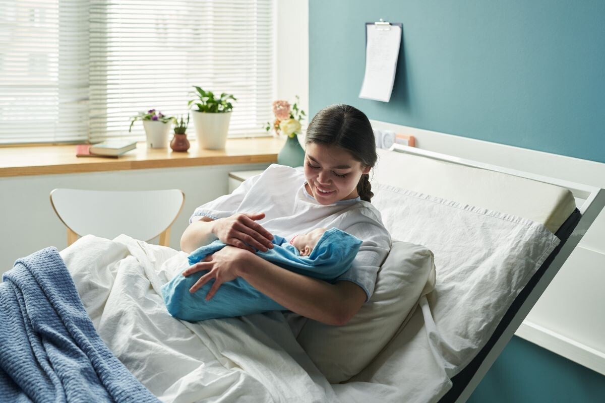 Lachende Mutter mit Neugeborenem im Krankenhausbett.