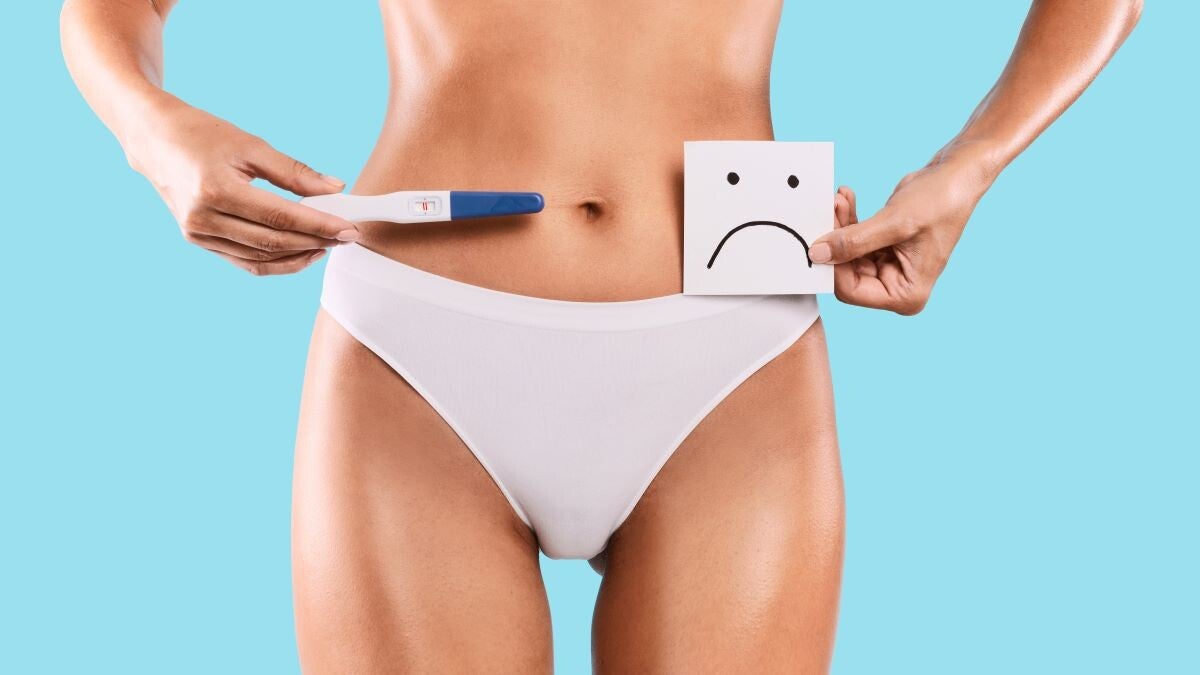 Frau hält Schwangerschaftstest und traurigen Smiley in der Hand