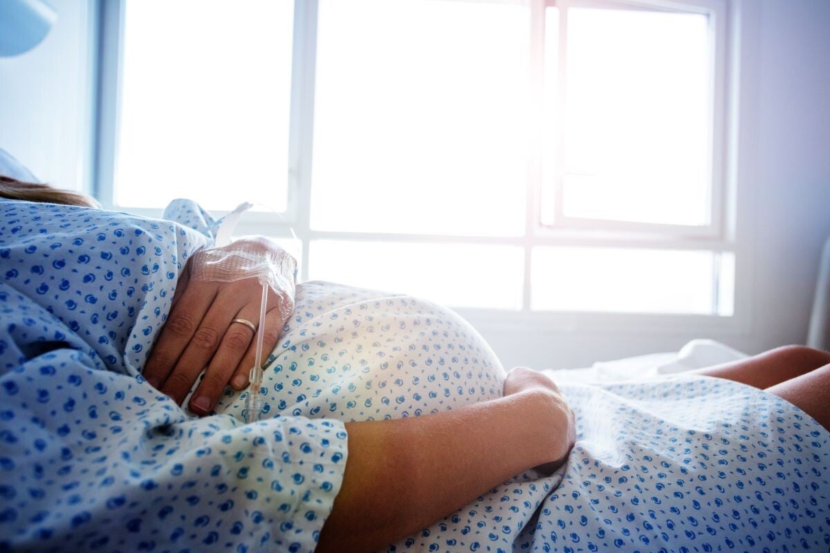  Schwangere Frau im Krankenhausbett hält Bauch.