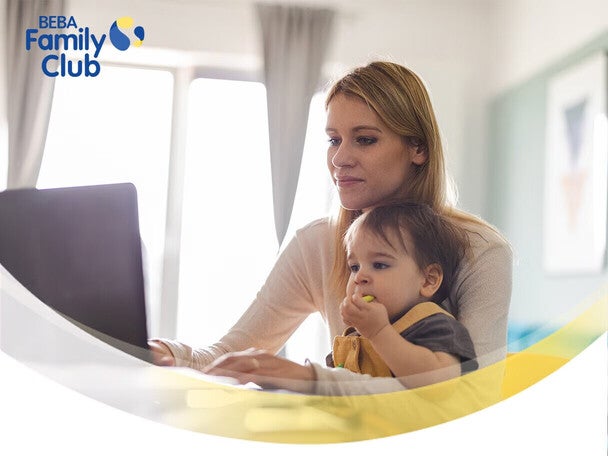 Mother and child at a table with a laptop, sunny window in the background.