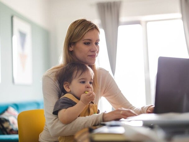 Eine Mutter hält ihr Kleinkind im Arm vor einem sonnenbeschienenen Fenster. Während sie das Kind liebevoll an sich drückt, hält sie ein Smartphone in der Hand.  Geben Sie Ihr Feedback zu BizChat ab.