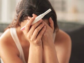 Eine Frau hält einen negativen Schwangerschaftstest und verdeckt aus Verzweiflung ihr Gesicht mit den Händen. 