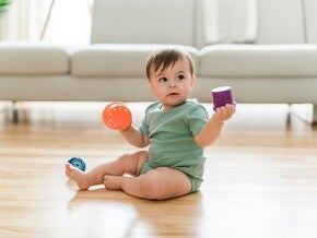 Baby sitzt auf dem Boden und spielt mit buntem Spielzeug