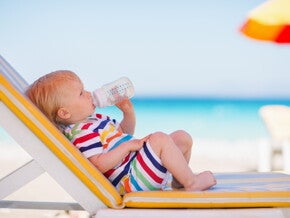 Baby trinkt aus Babyflasche während es auf einer Sonnenliege liegt