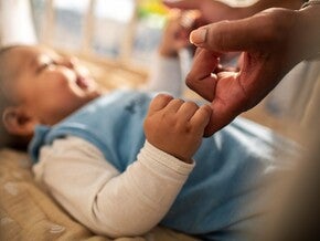 Baby hält mit der rechten Hand den Finger der Mutter fest und lächelt es an.