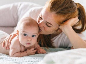 Mutter umarmt ihr Neugeborenes im Bett. Vier Monate altes Baby.