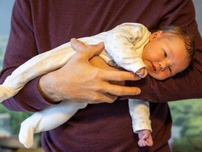 Nacktes Baby wird vom Vater im Fliegergriff gehalten.