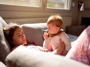 Mutter liegt mit ihrem Baby auf dem Sofa und schaut benommen