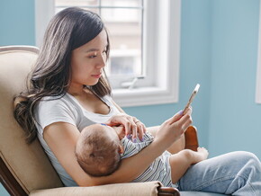 Mutter mit Baby im Arm, die auf ihr Telefon schaut