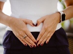 Schwangere Frau berührt ihren Bauch mit Händen in Herzform