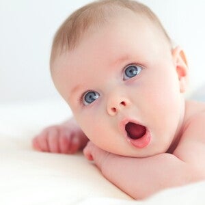 Baby schaut mit offenem Mund liegend in die Kamera
