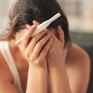 Eine Frau hält einen negativen Schwangerschaftstest und verdeckt aus Verzweiflung ihr Gesicht mit den Händen. 