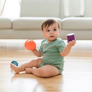Baby sitzt auf dem Boden und spielt mit buntem Spielzeug
