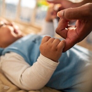 Baby hält mit der rechten Hand den Finger der Mutter fest und lächelt es an.