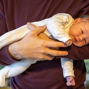 Nacktes Baby wird vom Vater im Fliegergriff gehalten.