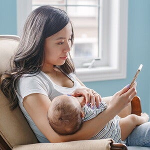 Mutter mit Baby im Arm, die auf ihr Telefon schaut