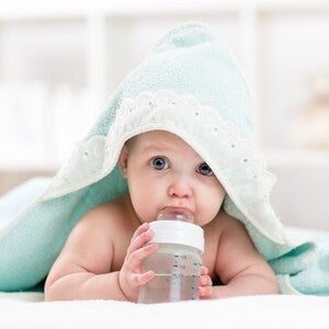 Baby hat ein Kapuzenhandtuch auf sich und liegt auf dem Bauch, während es an einer Flasche mit Wasser nuckelt.