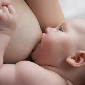Baby liegt auf dem Arm der Mutter und wird gestillt, während die Mutter die Hand des Babys hält.