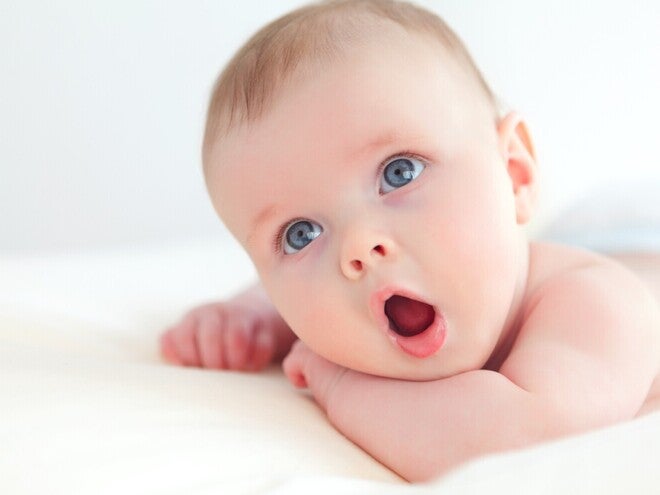 Baby schaut mit offenem Mund liegend in die Kamera
