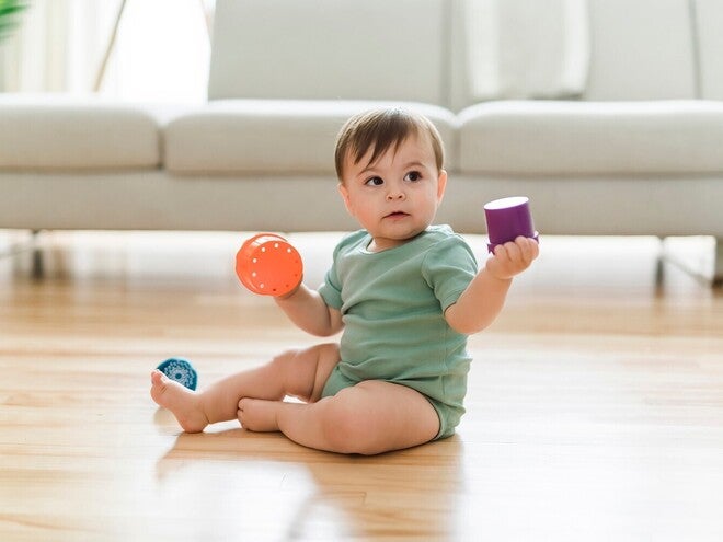Baby sitzt auf dem Boden und spielt mit buntem Spielzeug