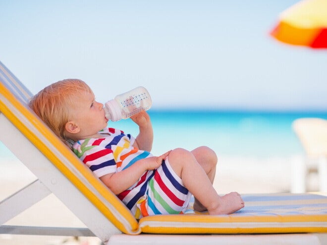 Baby trinkt aus Babyflasche während es auf einer Sonnenliege liegt