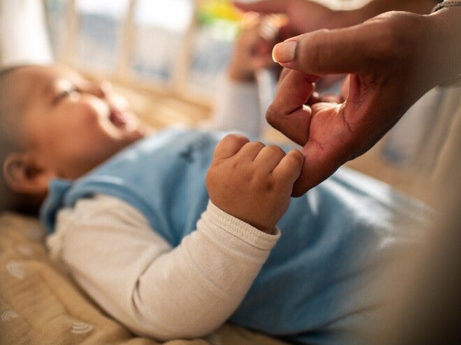 Baby hält mit der rechten Hand den Finger der Mutter fest und lächelt es an.