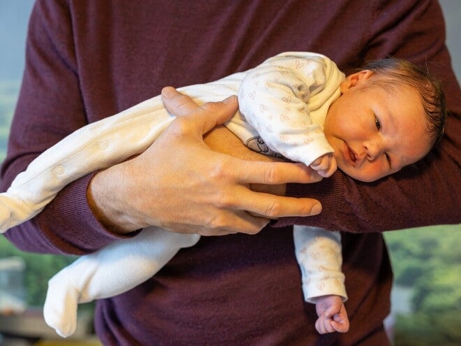 Nacktes Baby wird vom Vater im Fliegergriff gehalten.