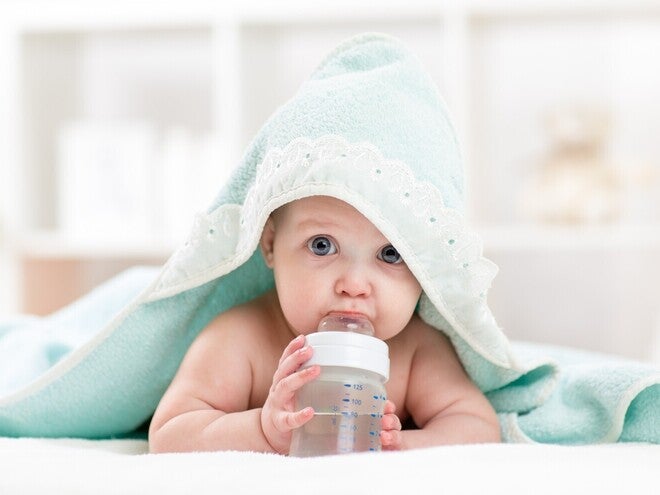 Baby hat ein Kapuzenhandtuch auf sich und liegt auf dem Bauch, während es an einer Flasche mit Wasser nuckelt.