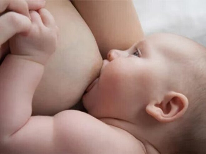 Baby liegt auf dem Arm der Mutter und wird gestillt, während die Mutter die Hand des Babys hält.