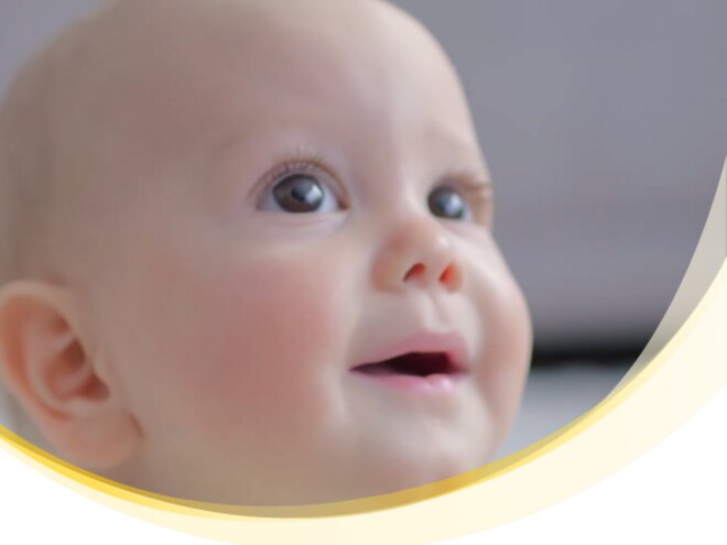 Kleiner Junge mit großen Augen, lächelt, heller Hintergrund.