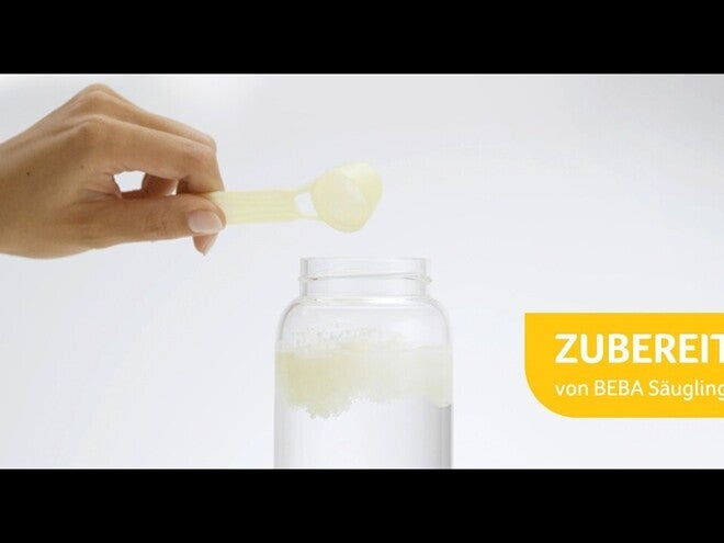 Frau hält Messlöffel mit Milchpulver über Glas.