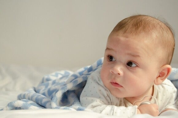 Ein Baby liegt auf dem Bauch und blickt aufmerksam zur Seite, zugedeckt mit einer blau-weißen Decke.