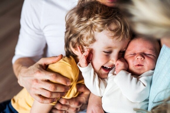 Ein Kleinkind lacht fröhlich, während es neben einem schlafenden neugeborenen Baby liegt.