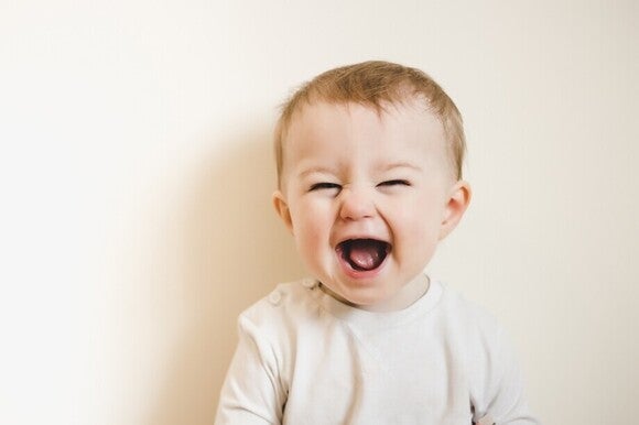 Ein lachendes Baby mit weit geöffnetem Mund schaut direkt in die Kamera.