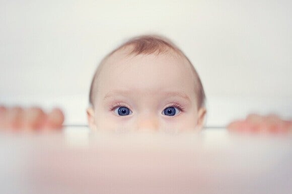 Baby schaut direkt in die Kamera und nur  ihr halbes Gesicht und ihre Hände sind sichtbar.