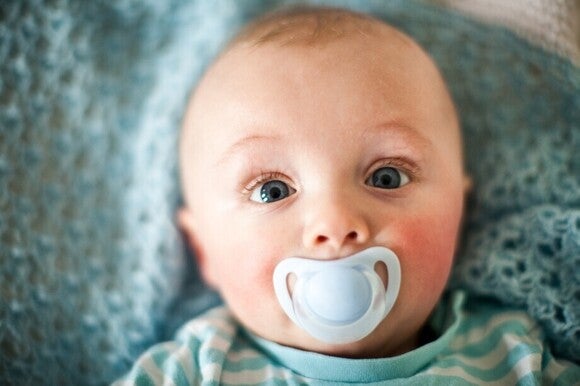 Baby schaut mit Schnuller im Mund ganz erstaunt nach oben.