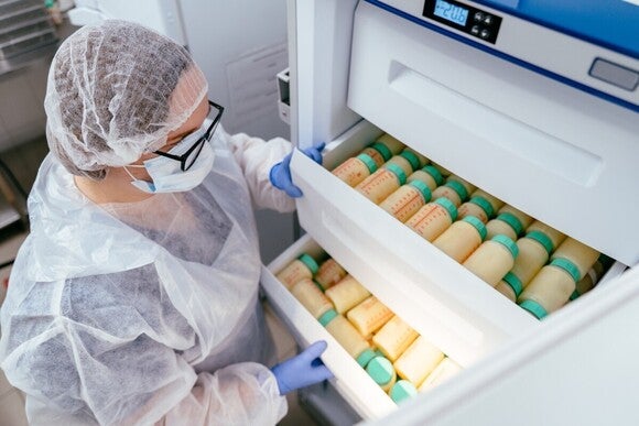 Forschende Person öffnet Schubladen eines Kühlungssystems voll mit kleinen Muttermilch-Flaschen.