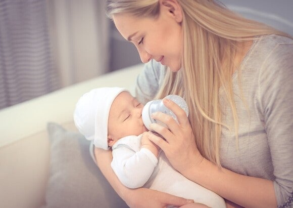 Mutter hält Baby auf dem Arm und stillt es mit einem Flässchen.