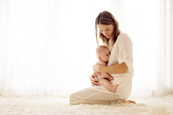 Mutter sitzt auf dem Boden und hält ihr Baby auf dem Schoß während es gestillt wird.