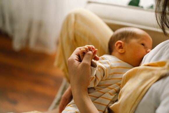 Das Baby liegt auf dem Arm und wird gestillt, während die Mutter die Hand des Babys hält.