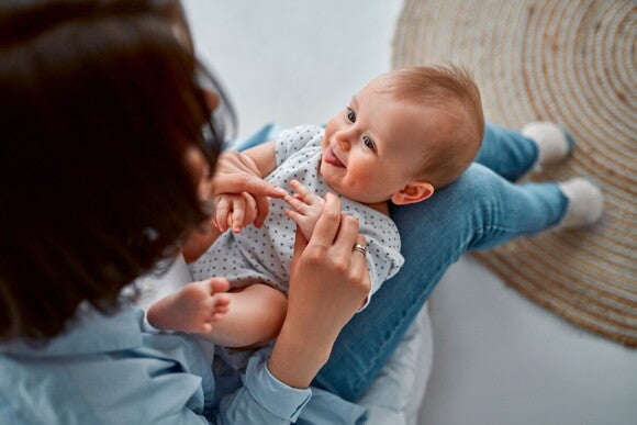 Baby liegt auf dem Schoss seiner Mutter und lächelt fröhlich Baby liegt auf dem Schoss seiner Mutter und lächelt fröhlich