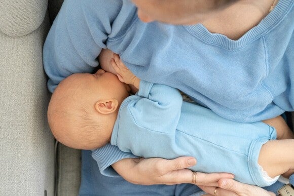 Bild in Vogelperspektive. Baby wird auf dem Arm gestillt. Mutter und Baby tragen hellblaue Kleidung.