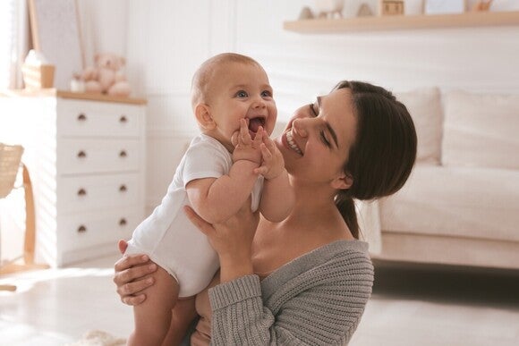 Baby auf dem Arm der Mutter. Beide lächeln in dem Moment.