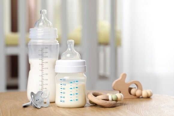 Zwei Babyflaschen gefüllt mit Milch in zwei unterschiedlichen Größen mit und einem Schnuller davor.