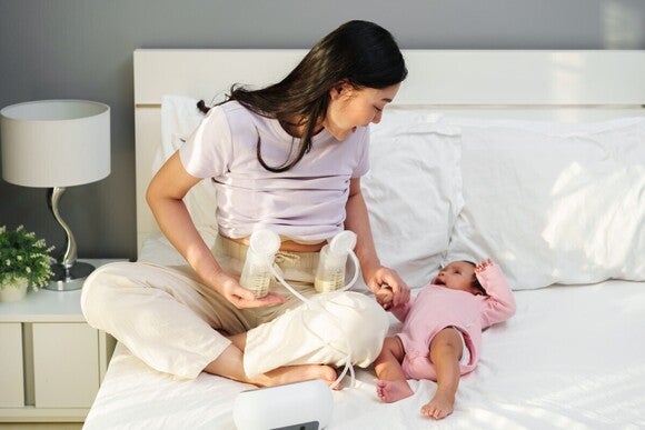 Mutter pumpt Muttermilch in die Babyflaschen ab während sie mit ihrem Baby spielt und es anlächelt.