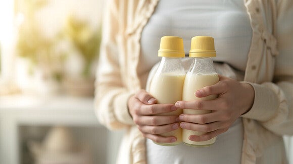 Mutter hält zwei volle Milchflaschen voll mit Muttermilch dicht an ihrem Bauch mit zwei Händen.