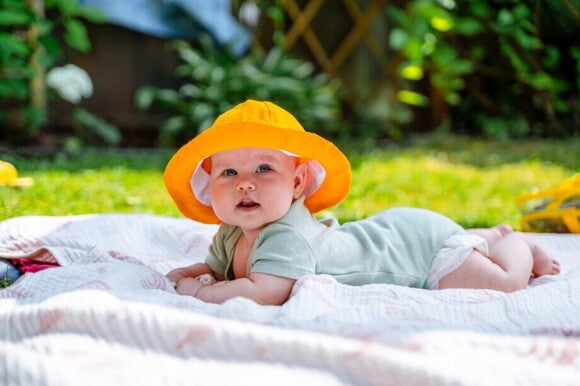 Baby mit großem Sommerhut liegt im Garten auf einer Sommerdecke Baby mit großem Sommerhut liegt im Garten auf einer Sommerdecke