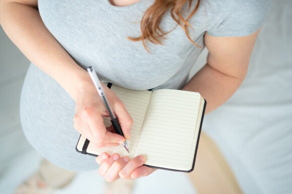 Schwangere Frau macht sich Notizen in einem Notizbuch Schwangere Frau macht sich Notizen in einem Notizbuch
