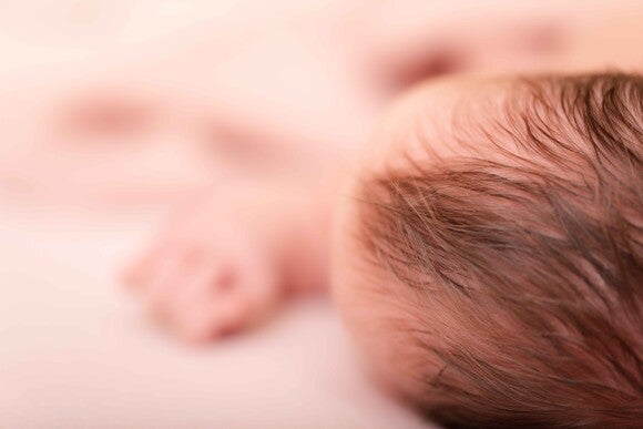 Newborn baby lying on a soft pink blanket, seen from above.