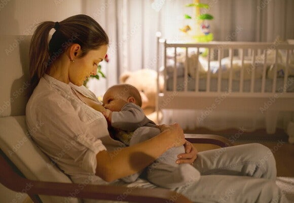 Baby liegt nachts an Brust der Mutter und wird gestillt Baby liegt nachts an Brust der Mutter und wird gestillt